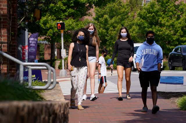 Four college students wearing masks walk down a brick path