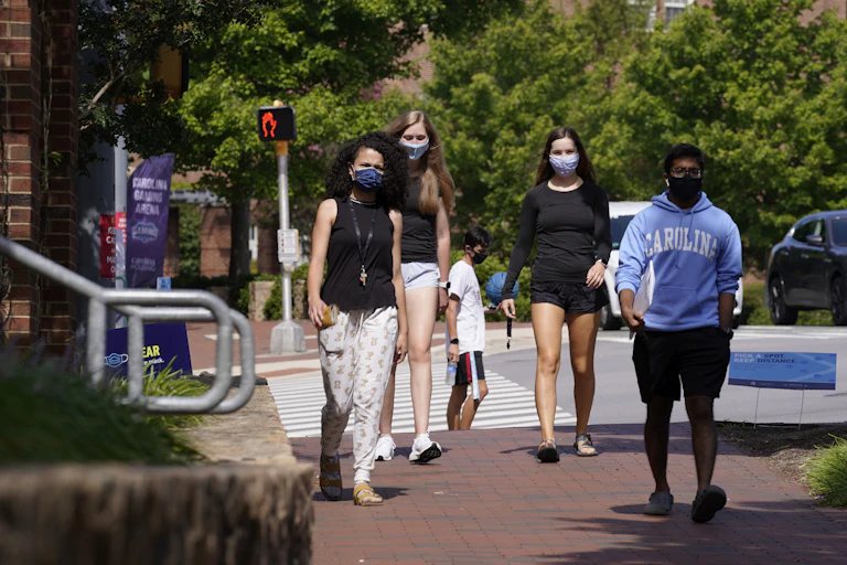 Four college students wearing masks walk down a brick path