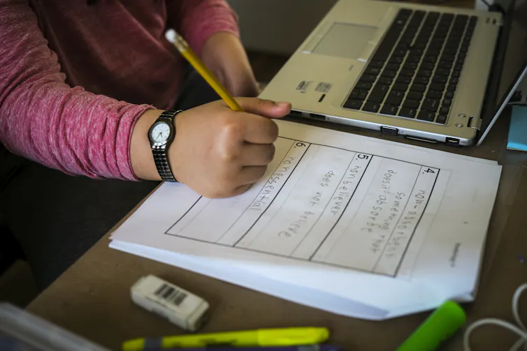 A child sitting in front of a computer and working with a pencil and paper