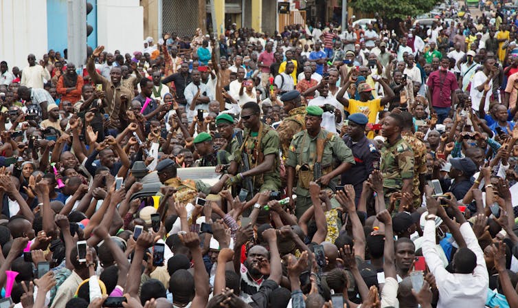 Crowd of supporters raising their fists and snapping photos of soldiers in fatigues