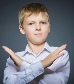 A boy in while shirt crossing his arms in front of him into an x shape.