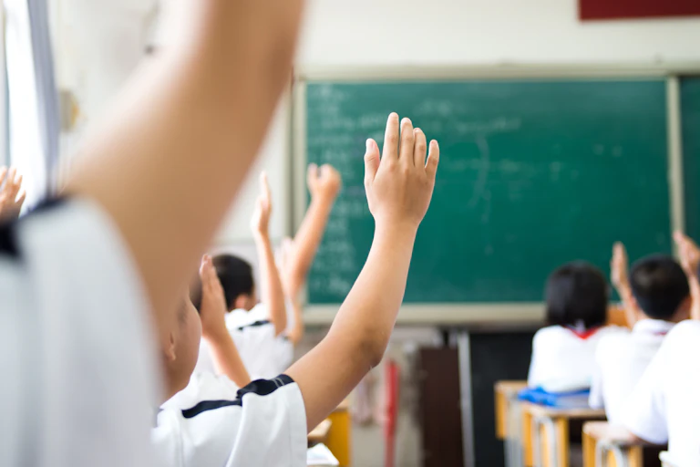 Classroom scene with hands raised.