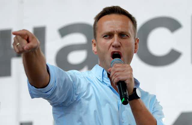 Alexei Navalny speaks into a microphone. His arm is outstretched and he is pointing his finger.