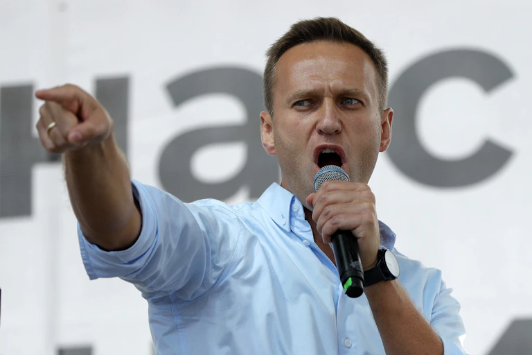 Alexei Navalny speaks into a microphone. His arm is outstretched and he is pointing his finger.