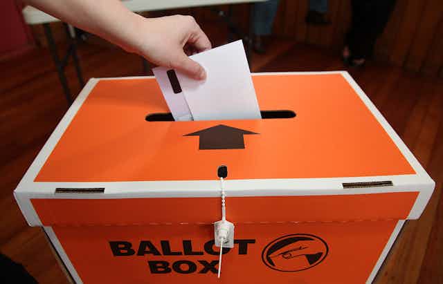 orange ballot box with hand holding voting paper