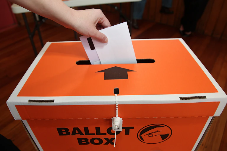 orange ballot box with hand holding voting paper