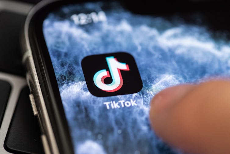 Thumb hovering over TikTok icon on phone screen