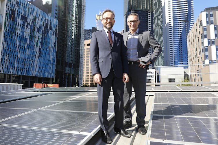 Adam Bandt and Richard Di Natale standing against a Melbourne city skyline.