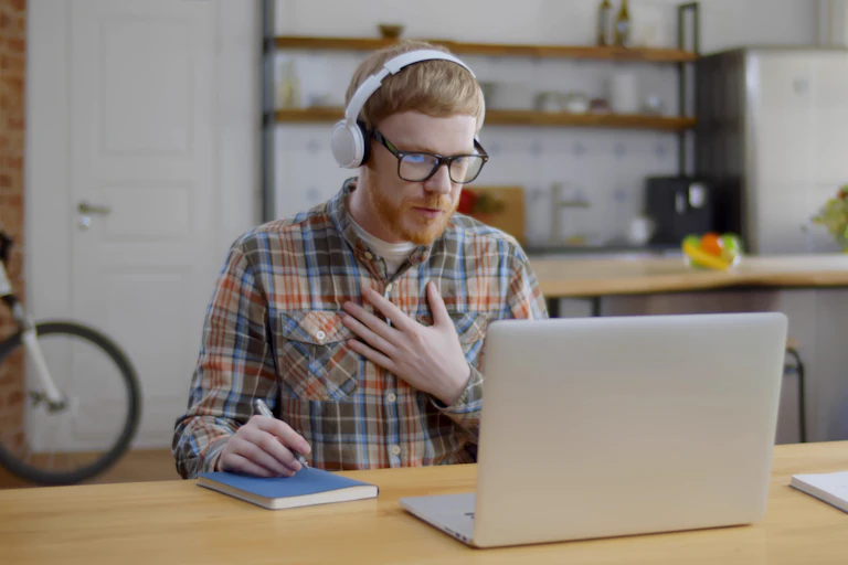A man looking anxious as he takes part in a video hook up with colleagues, via a laptop on a table at home.