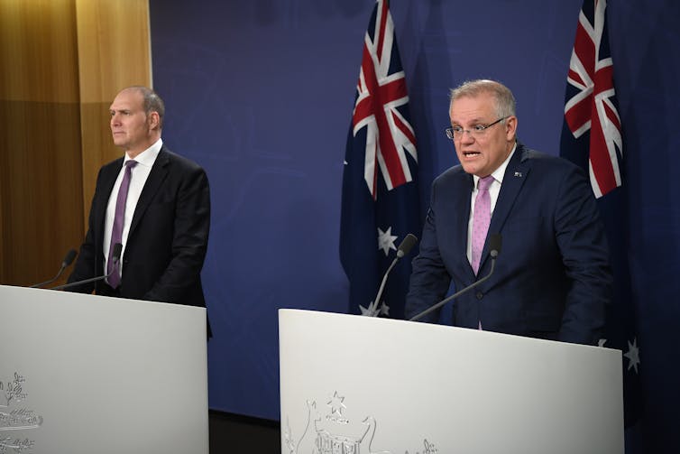 Nev Power and Scott Morrison behind a podium giving a press conference.