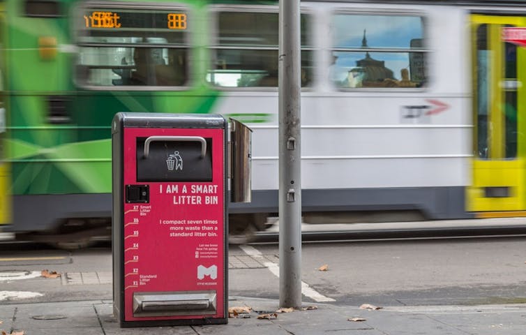 Smart litter bin on pavement with a Melbourne tram passing behind it