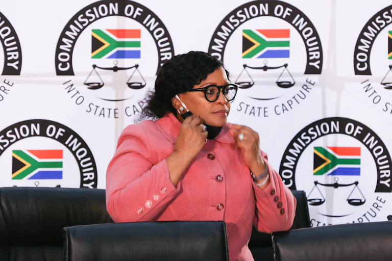 Nomvula Mokonyane in front of state capture commission logos