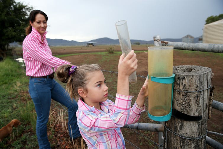 A young girl checks a rain gauge