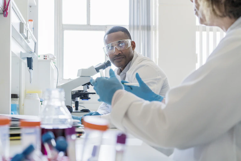 A photo of chemist looking at colleague while working in laboratory.