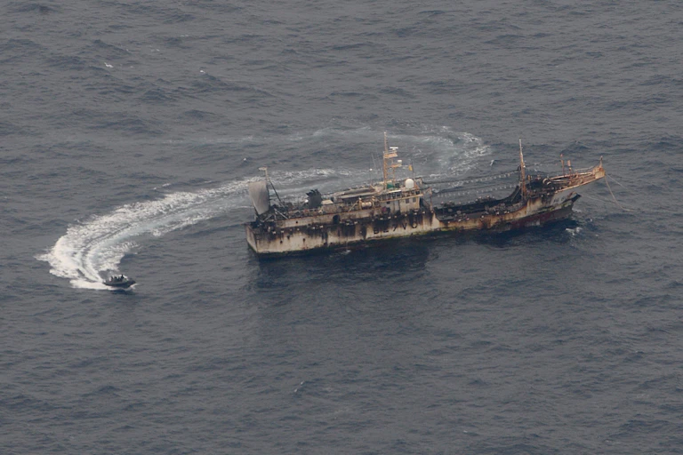 A small ship circles a much larger ship in the ocean