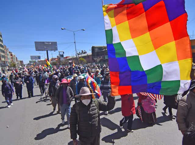 Protestors waving colourful flags walk down a street.