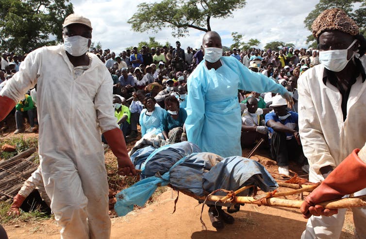 Men in surgical masks carry body on a stretcher.