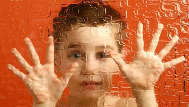 Manos y cara de un niño tras un cristal esmerilado.