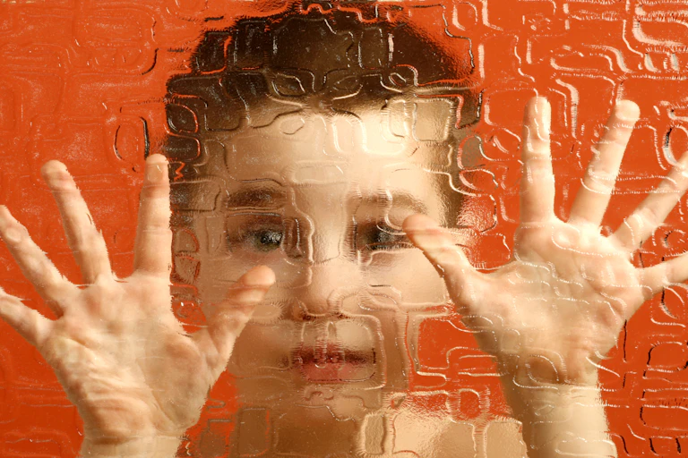 Manos y cara de un niño tras un cristal esmerilado.