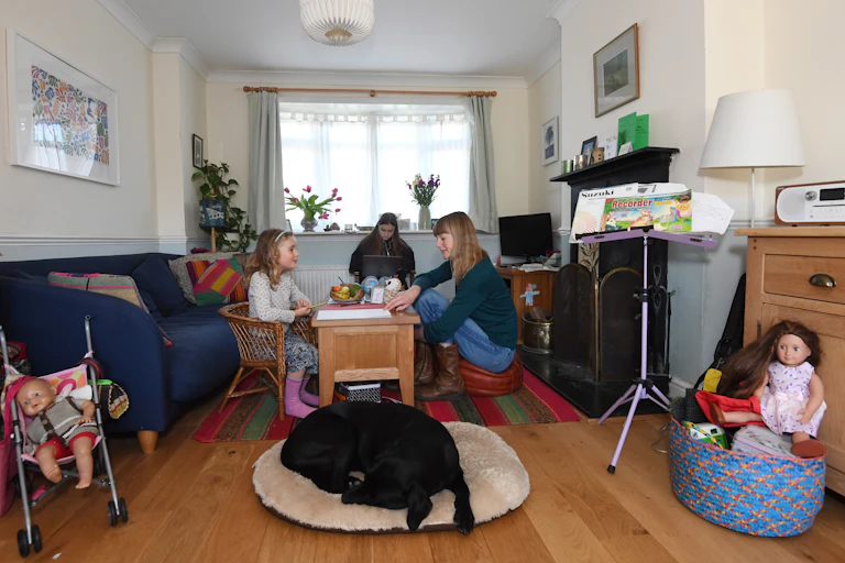 A mother teaches her children at home while a labrador sleeps by the table.