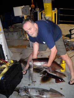 A man holding red devil squids with others on the ship deck