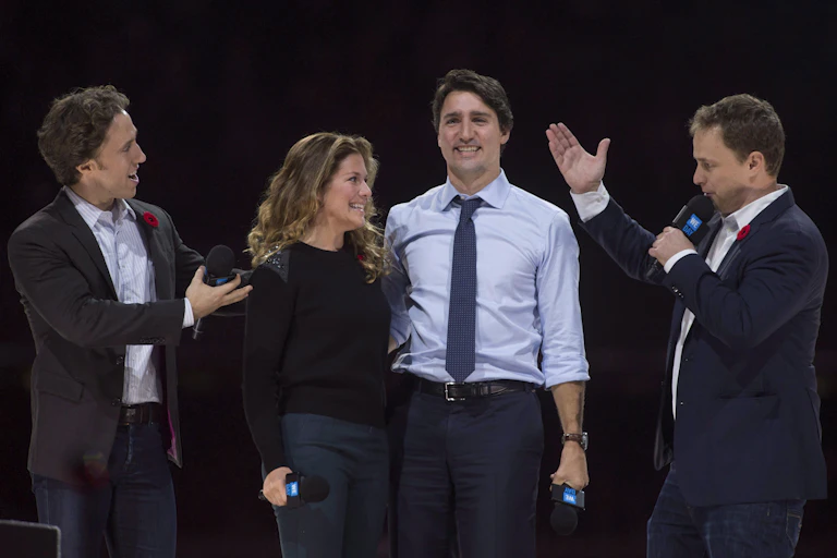 Craig Kielburger stands to the right of Sophie Gregoire-Trudeau and Justin Trudeau on a stage, with his brother Marc to their left.