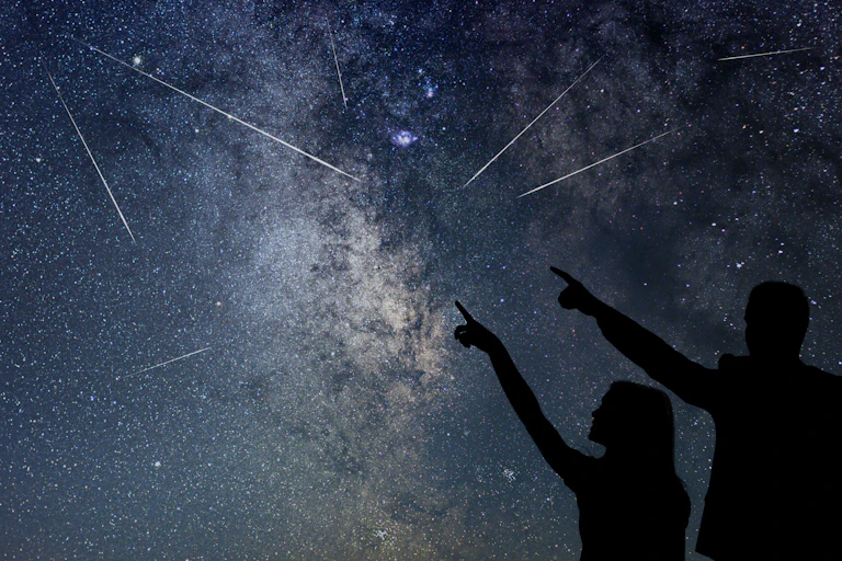 Two people point and look at shooting stars flying through the night sky.