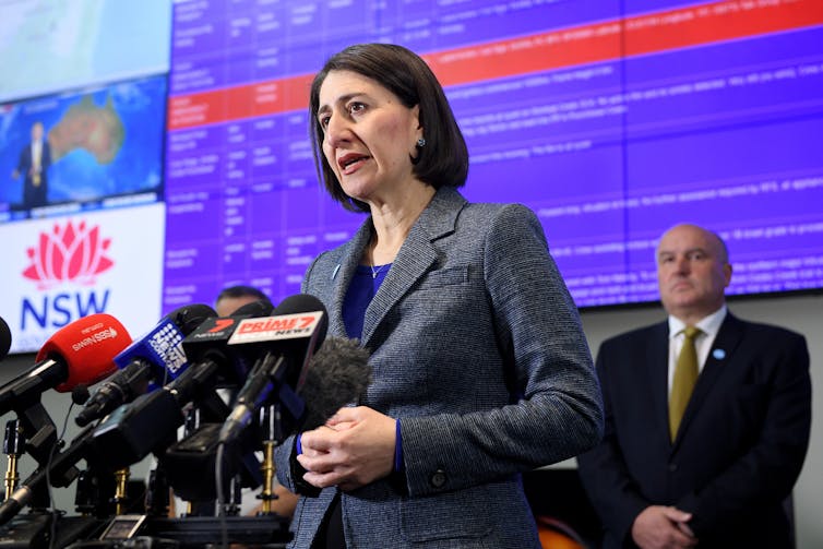 Gladys Berejiklian stands behind a podium at a press conference.