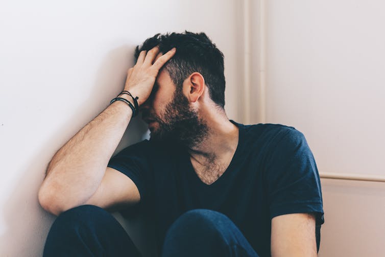 Man sits against the wall with his head in his hand.