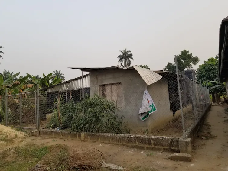A simple breezeblock brick structure with a fence around it, its zinc roof buckling and a faded poster hanging from the fence.