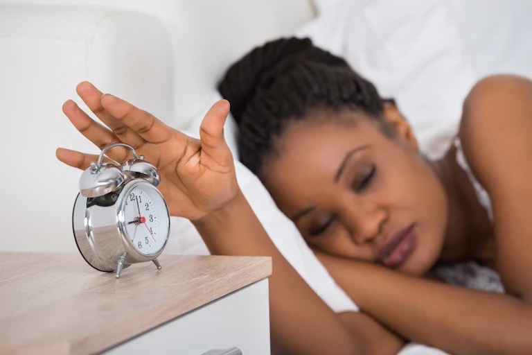 Sleeping woman reaches for alarm clock.