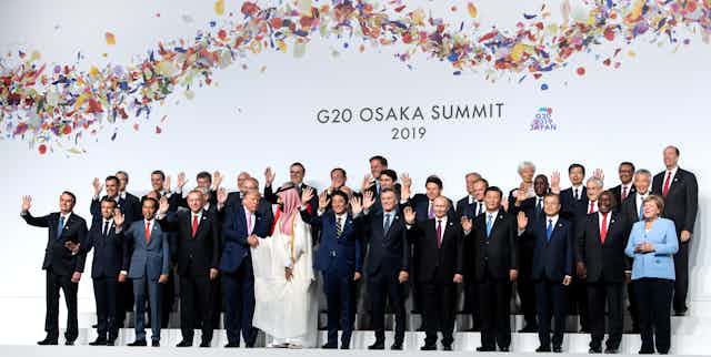 World leaders wave for a group photo at the G20 meeting while Trump shakes hands with the Saudi leader