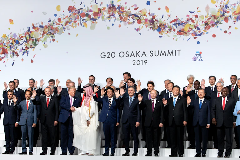 World leaders wave for a group photo at the G20 meeting while Trump shakes hands with the Saudi leader