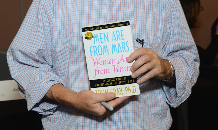 A man holds a copy of 'Men Are from Mars, Women Are from Venus.'