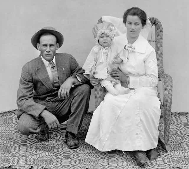 A stern-looking husband and wife pose with their child.