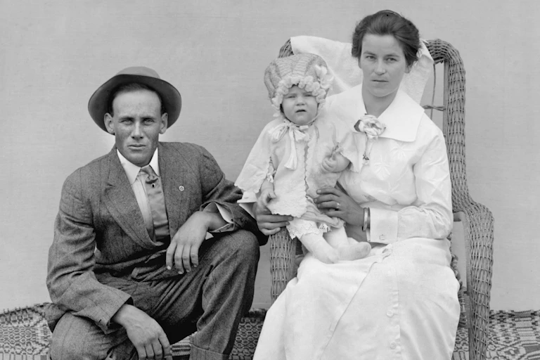 A stern-looking husband and wife pose with their child.
