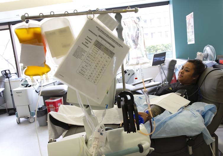 A young woman lies in a hospital bed donating plasma.