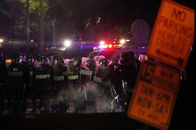 Police in riot gear stand behind shields