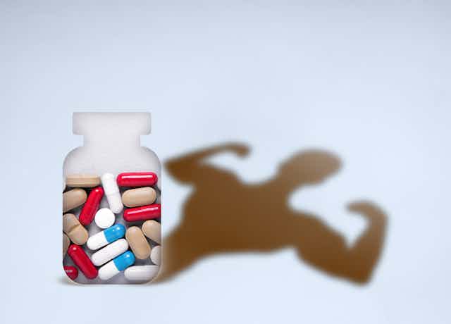 A bottle of pills casts a shadow in the shape of a body builder's torso flexing its biceps.