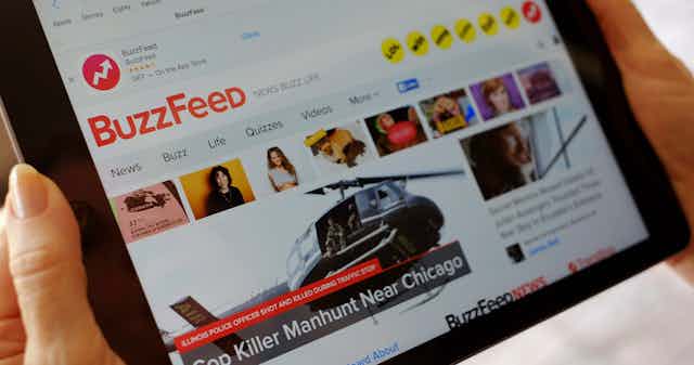 A woman holds a tablet with the Buzzfeed home page displayed.