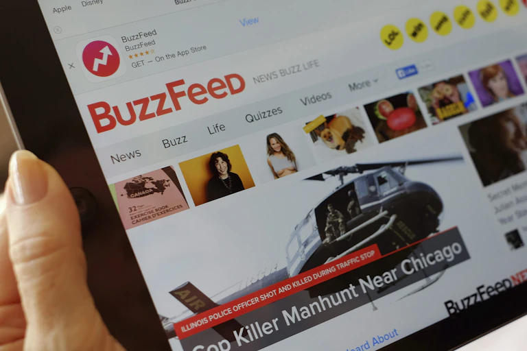A woman holds a tablet with the Buzzfeed home page displayed.