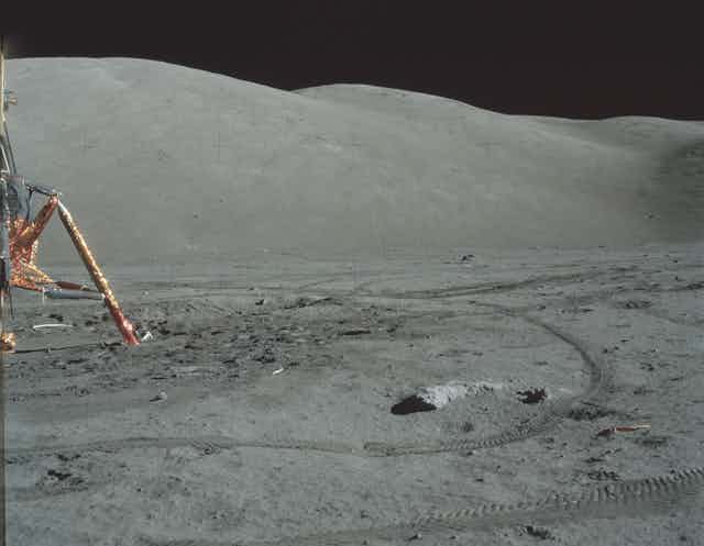 A golden lunar lander and tyre tracks on the Moon.