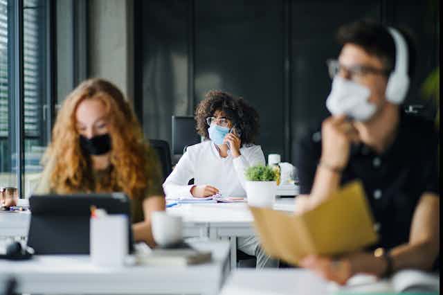Three young adults wearing masks in office environment.