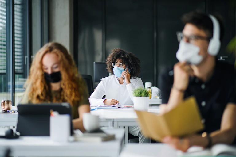 Three young adults wearing masks in office environment.