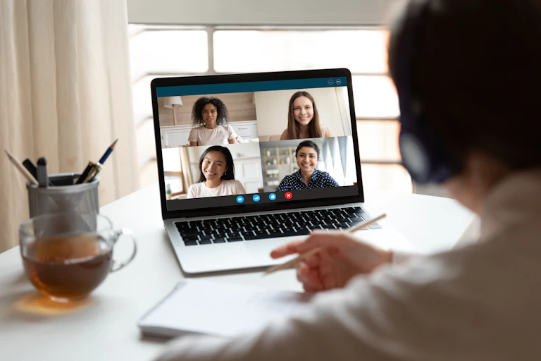 Young women looking at laptop screen showing four others in online chat