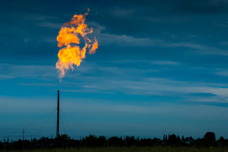 Gas burning from a tall factory pipe on a dark and dusky day.