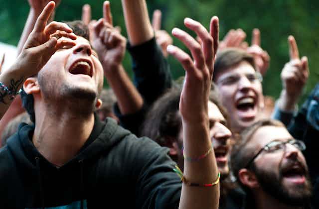 Young people in a crowd lifting their hands up as they sing