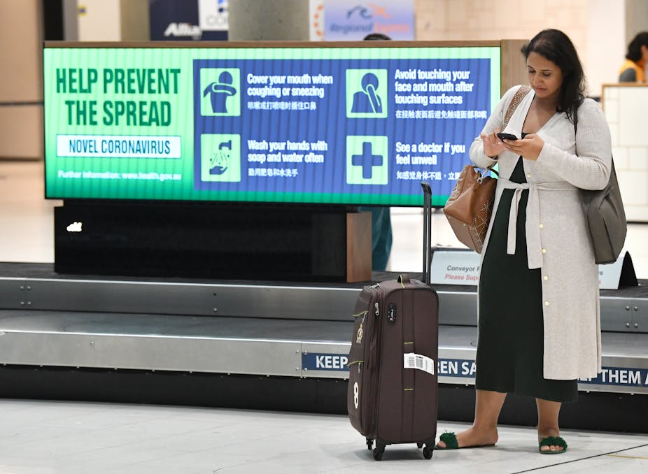 Woman checking phone, standing next to bag at empty airport
