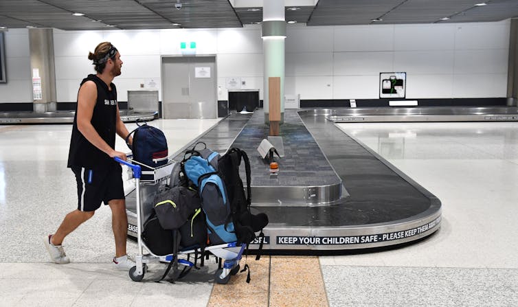 Man pushing a baggage trolly past an empty airport carousel.