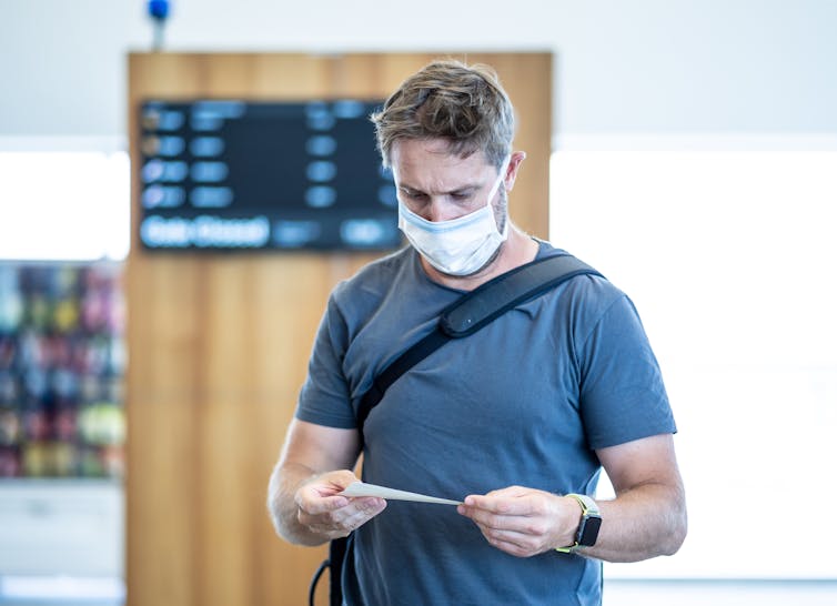Man in mask at airport, looking at ticket.